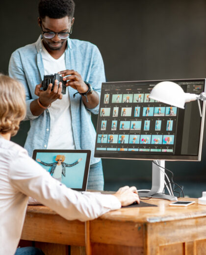 Two male photographers choosing woman's portraits at the working place with two computers in the studio